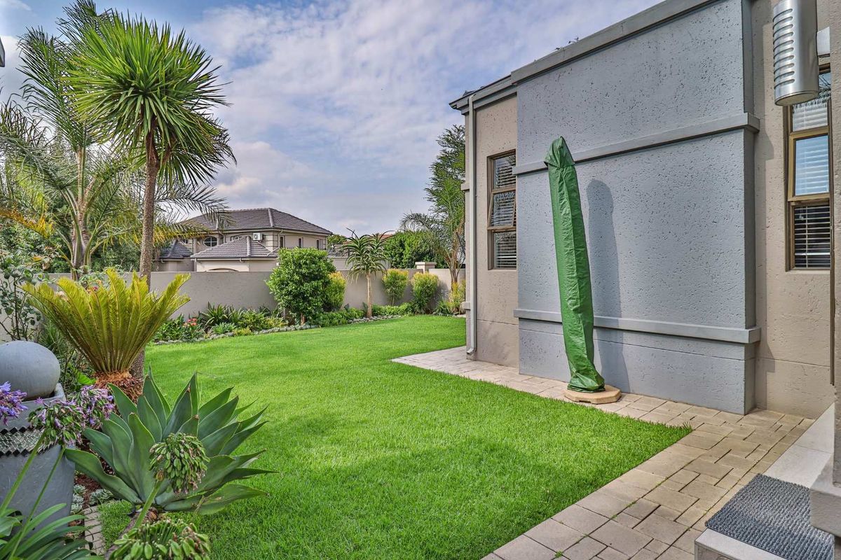 A well-maintained rear garden featuring a manicured lawn, paved walkway, and established landscaping alongside the exterior wall of the house.