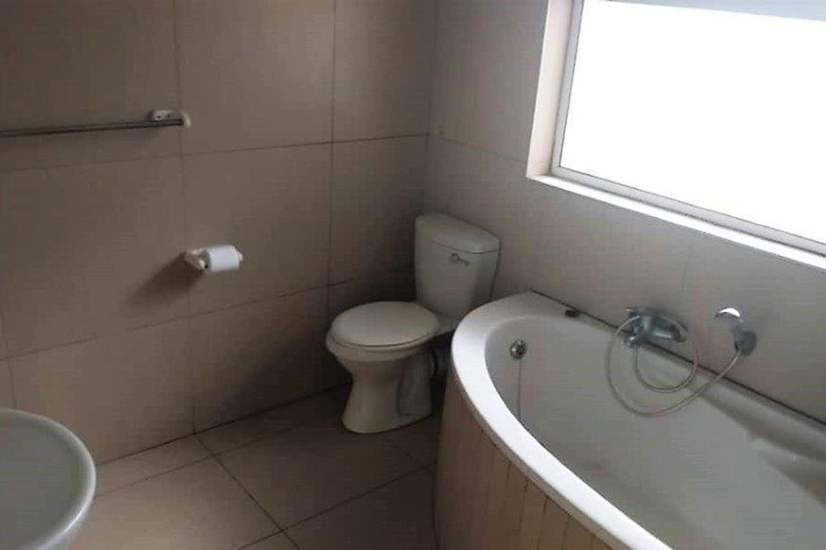 A functional bathroom featuring a built-in bathtub with shower mixer, a standard toilet, and tiled walls and flooring.