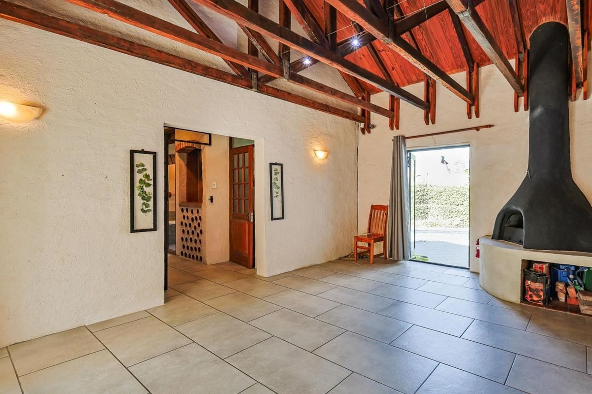 Spacious living area featuring exposed timber roof trusses, tiled flooring, and a prominent built-in fireplace, with direct access to the outdoor patio.