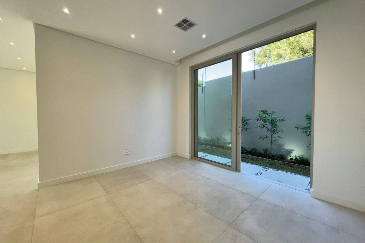 A bright, modern, and empty living space featuring large sliding glass doors that open onto a private, landscaped courtyard area.