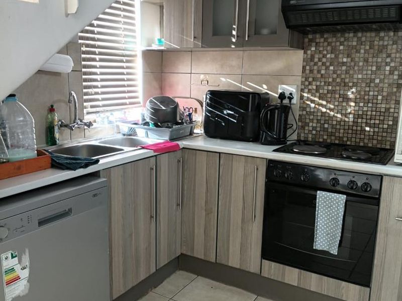 Compact kitchen featuring wood-look cabinetry, mosaic tile backsplash, built-in oven with extractor fan, and tiled flooring, situated beneath a staircase.