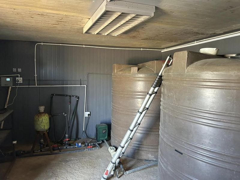 Utility room featuring large water storage tanks, a pump system, and exposed electrical infrastructure with timber ceiling finishes.