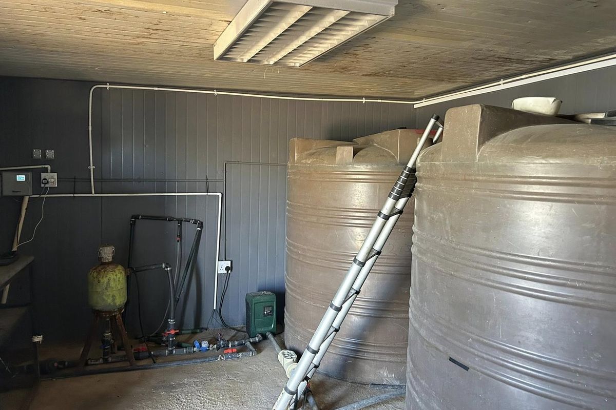 Utility room featuring large water storage tanks, a pump system, and exposed electrical infrastructure with timber ceiling finishes.