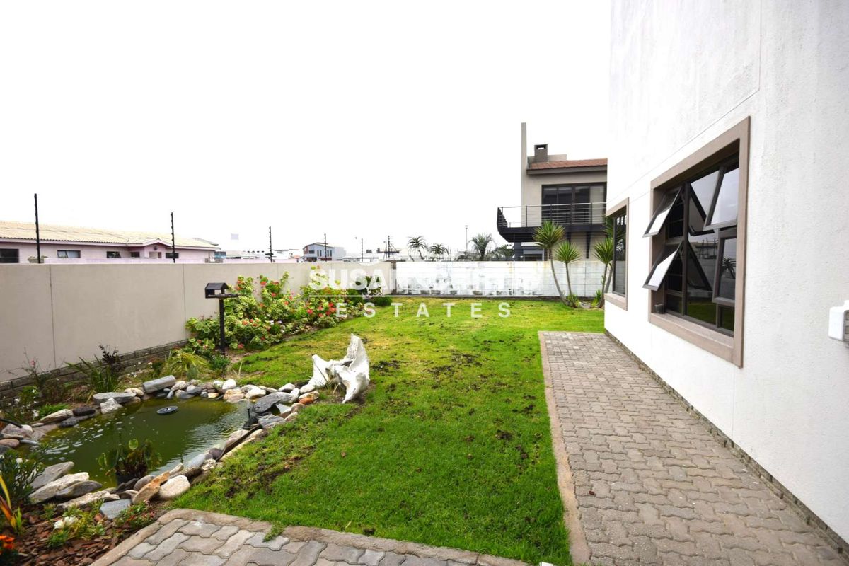 A rear garden area featuring a paved walkway, a small decorative pond, and a perimeter boundary wall.
