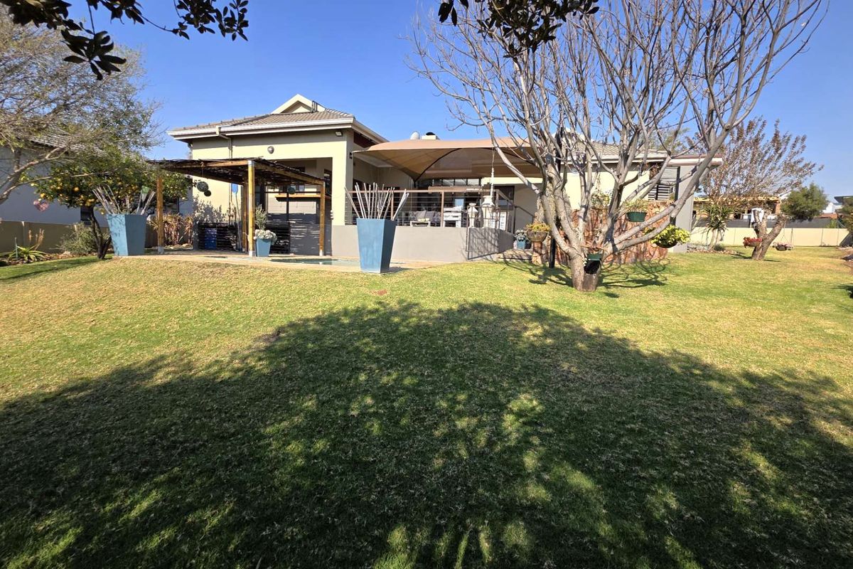 Rear view of the property featuring a landscaped garden, swimming pool, and a covered patio area with a shade sail.