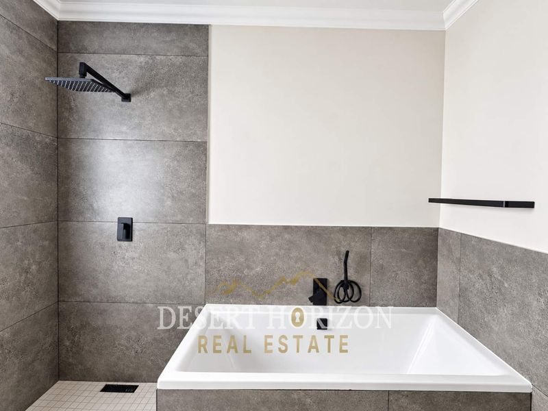 Modern bathroom featuring a built-in bathtub, integrated shower system, and contemporary matte black fixtures with large-format grey wall tiles.