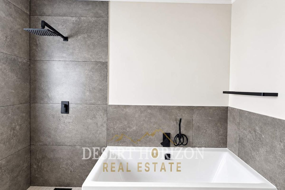 Modern bathroom featuring a built-in bathtub, integrated shower system, and contemporary matte black fixtures with large-format grey wall tiles.
