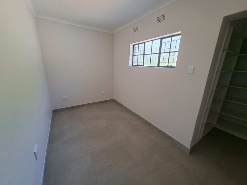 A clean, empty bedroom featuring neutral tiled flooring, built-in shelving, and a window with security bars.