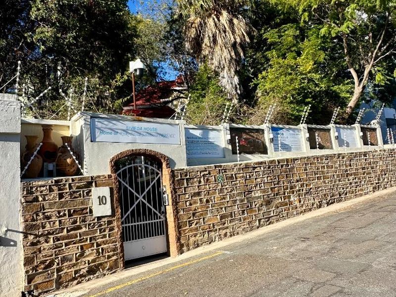 Front exterior view of the property featuring a stone masonry boundary wall, security gate, and electric fencing.