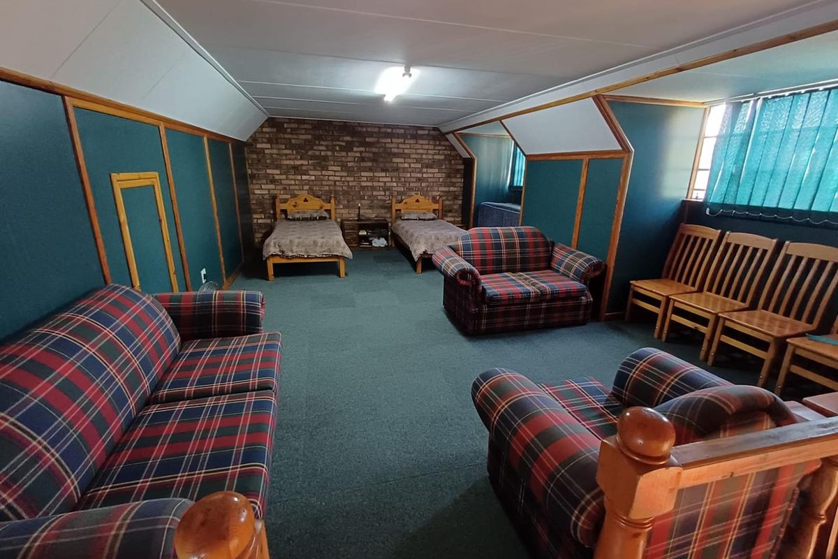 Spacious bedroom featuring exposed brick feature wall, dark green wall paneling, and carpeted flooring, offering a versatile layout with multiple sleeping and seating areas.