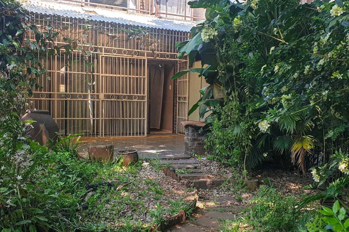 Rear exterior view of the property featuring a stone pathway leading to a covered patio area with security gates and a balcony above.