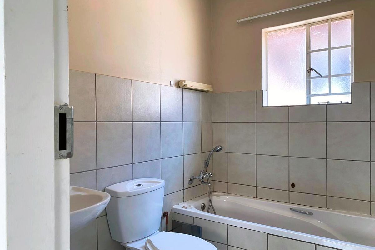 A functional bathroom featuring a standard bathtub with shower mixer, a white toilet, and a wall-mounted basin with neutral wall tiling.