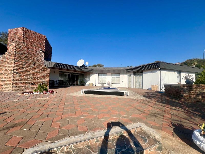 Spacious rear patio area featuring brick paving, a swimming pool with cover, and direct access to the home via multiple sliding glass doors.