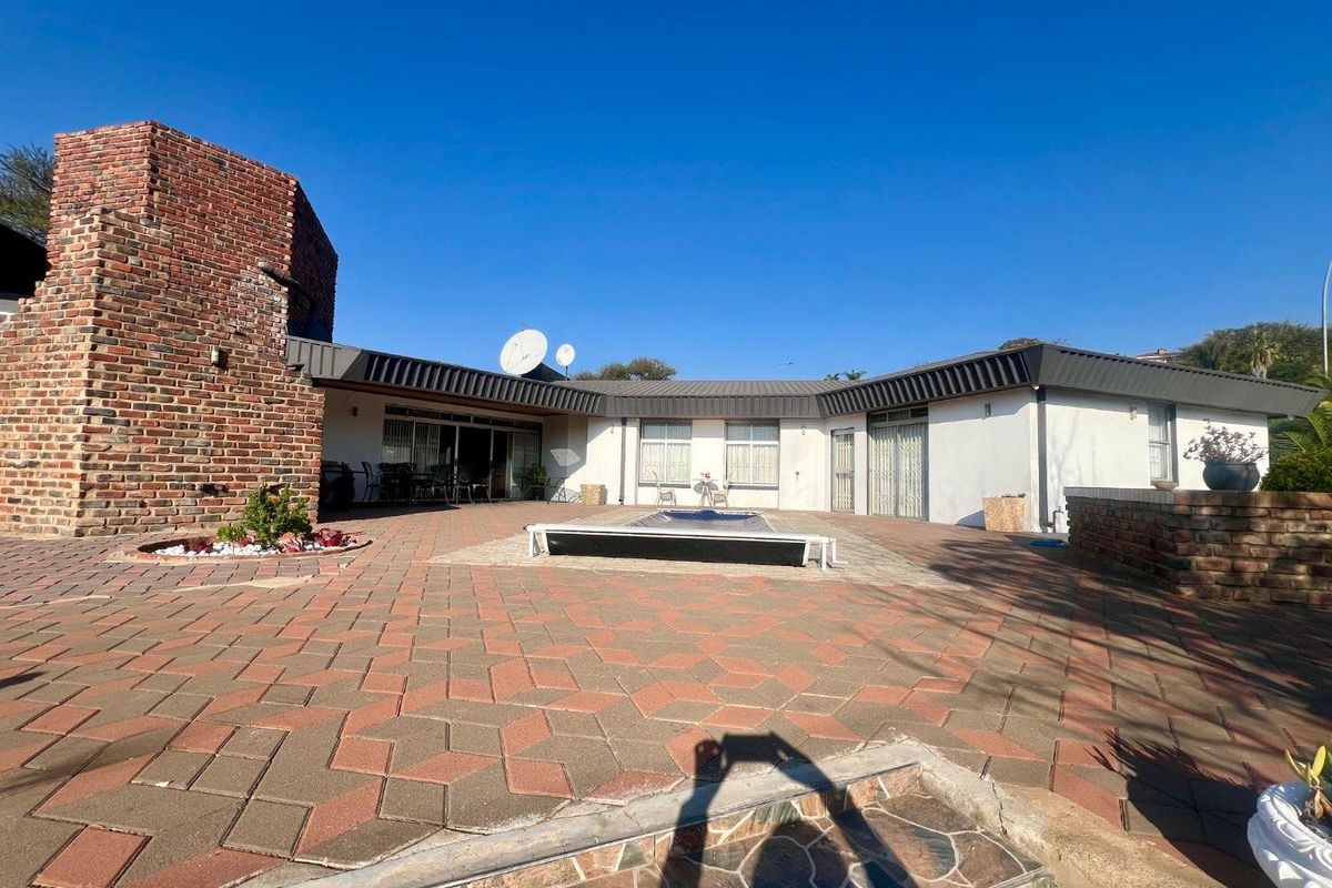 Spacious rear patio area featuring brick paving, a swimming pool with cover, and direct access to the home via multiple sliding glass doors.