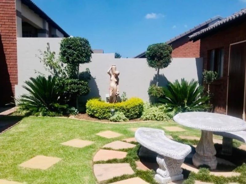 A well-maintained rear garden area featuring a manicured lawn, paved stepping stones, and a brick boundary wall in a cluster home setting.