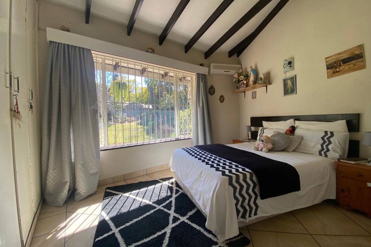 A bedroom featuring vaulted ceilings with exposed timber beams, tiled flooring, built-in cupboards, and a wall-mounted air conditioning unit.