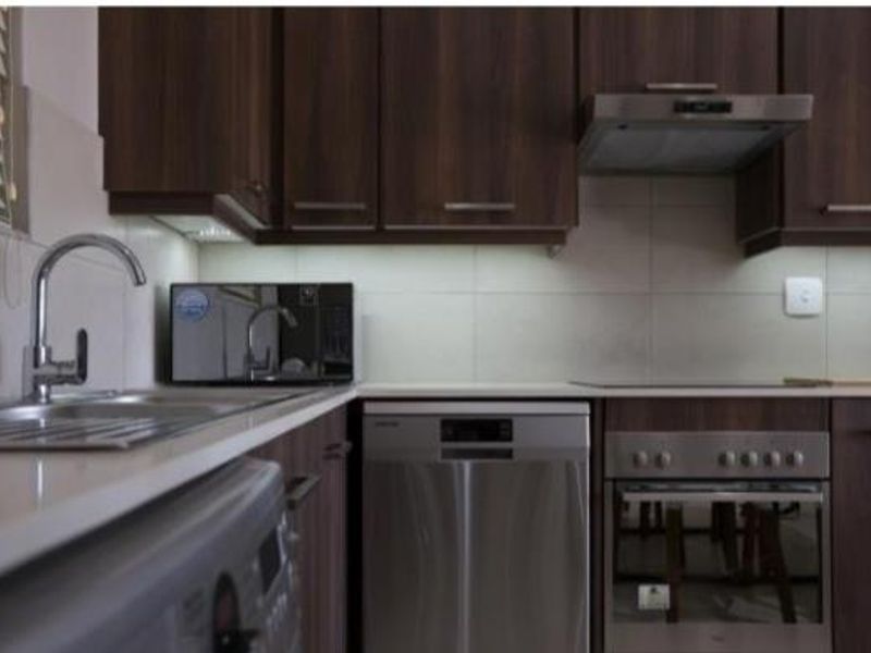 Modern kitchen featuring dark wood cabinetry, stone countertops, stainless steel appliances, and a tiled backsplash.