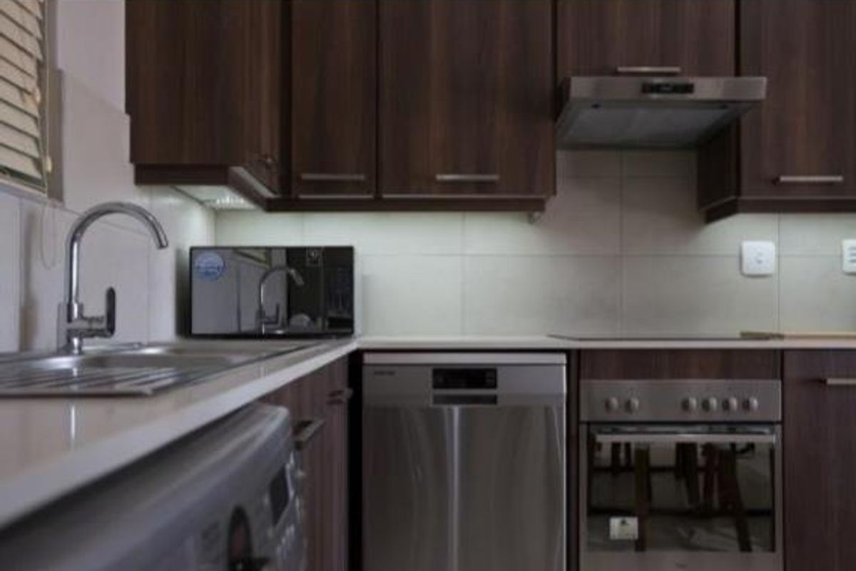 Modern kitchen featuring dark wood cabinetry, stone countertops, stainless steel appliances, and a tiled backsplash.