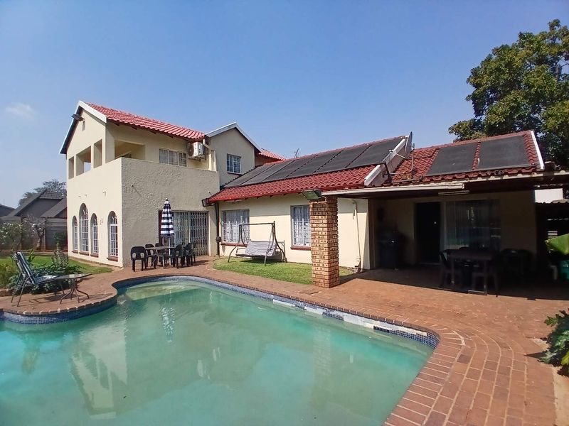 Rear view of the house featuring a swimming pool with solar heating panels, a brick patio area, and a multi-level exterior facade.