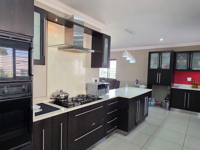 Modern kitchen featuring dark wood cabinetry, stone countertops, built-in oven, gas hob, and an extractor fan with tiled flooring and recessed lighting.