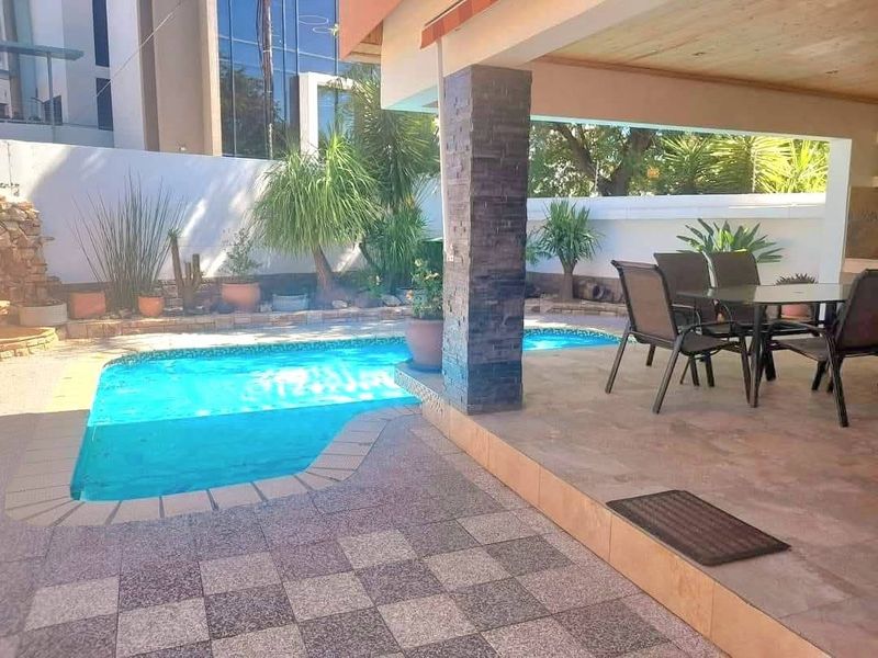 Outdoor entertainment area featuring a swimming pool, stone-clad pillar, and a covered patio space, ideal for relaxation and hosting.