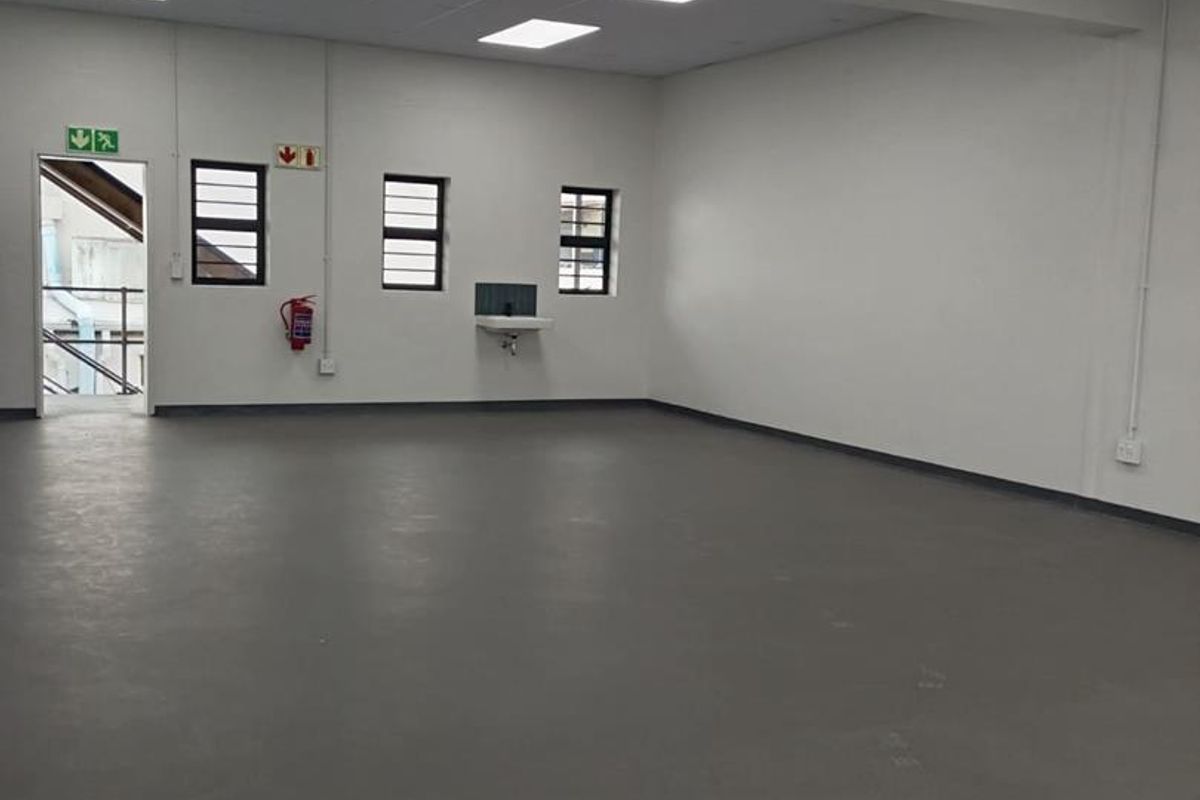 A clean, open-plan industrial utility space featuring durable epoxy flooring, suspended ceiling with recessed lighting, and a wall-mounted basin.