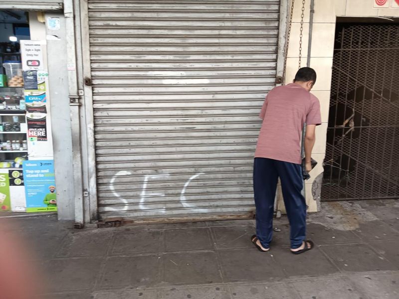 Street-level view of a commercial storefront featuring a metal roller shutter door and adjacent security gate entrance.