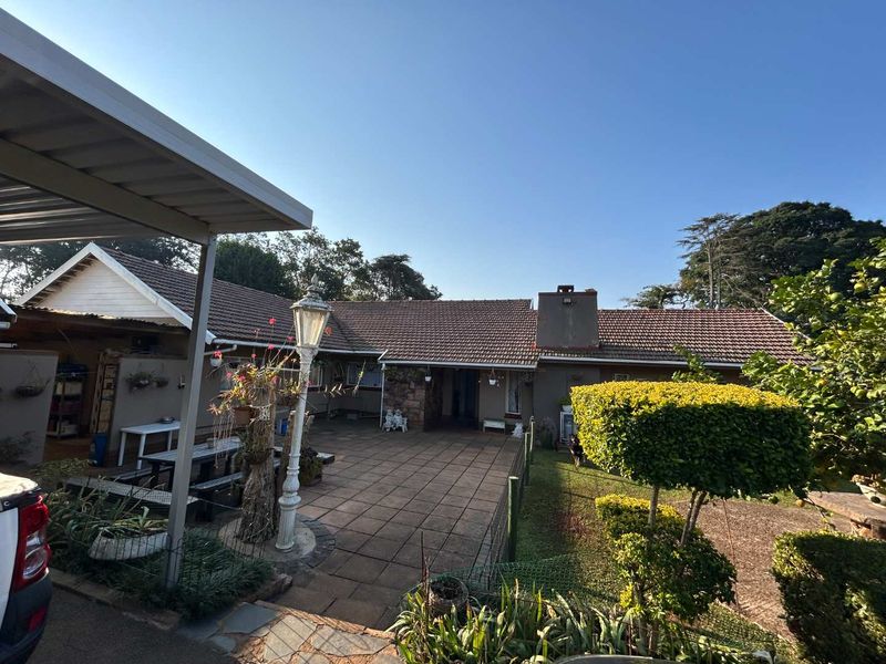 Rear view of the property featuring a paved patio area, covered carport, and a brick chimney, set against a garden backdrop.
