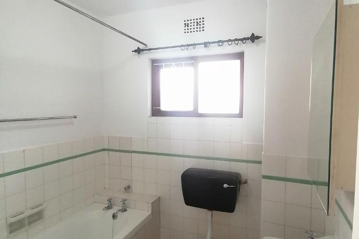 A dated bathroom featuring a standard bathtub, wall-mounted toilet, and washbasin with tiled walls and a window for natural light.