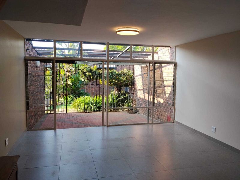 Spacious living area featuring large glass sliding doors that open onto a private brick-paved patio and garden, with neutral tiled flooring throughout.