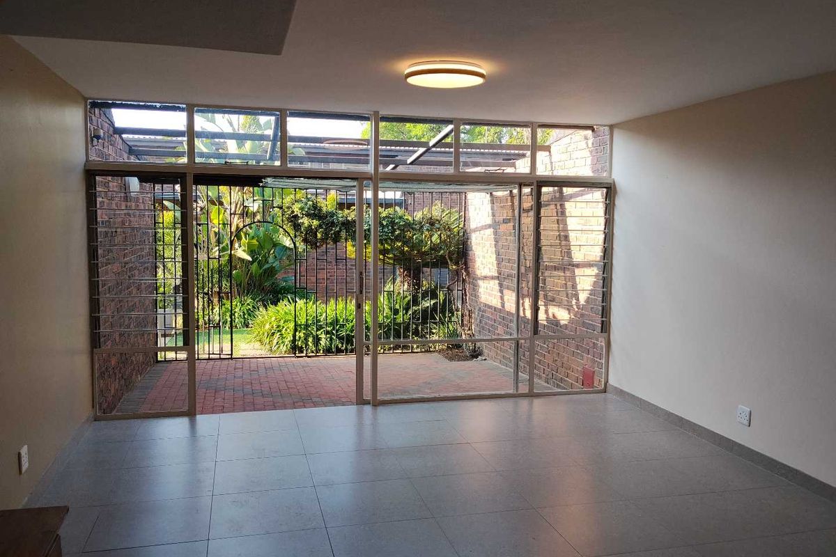 Spacious living area featuring large glass sliding doors that open onto a private brick-paved patio and garden, with neutral tiled flooring throughout.