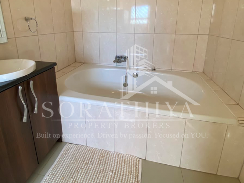 A functional bathroom featuring a built-in vanity with a basin and a tiled bathtub surround, offering a clean and neutral layout.