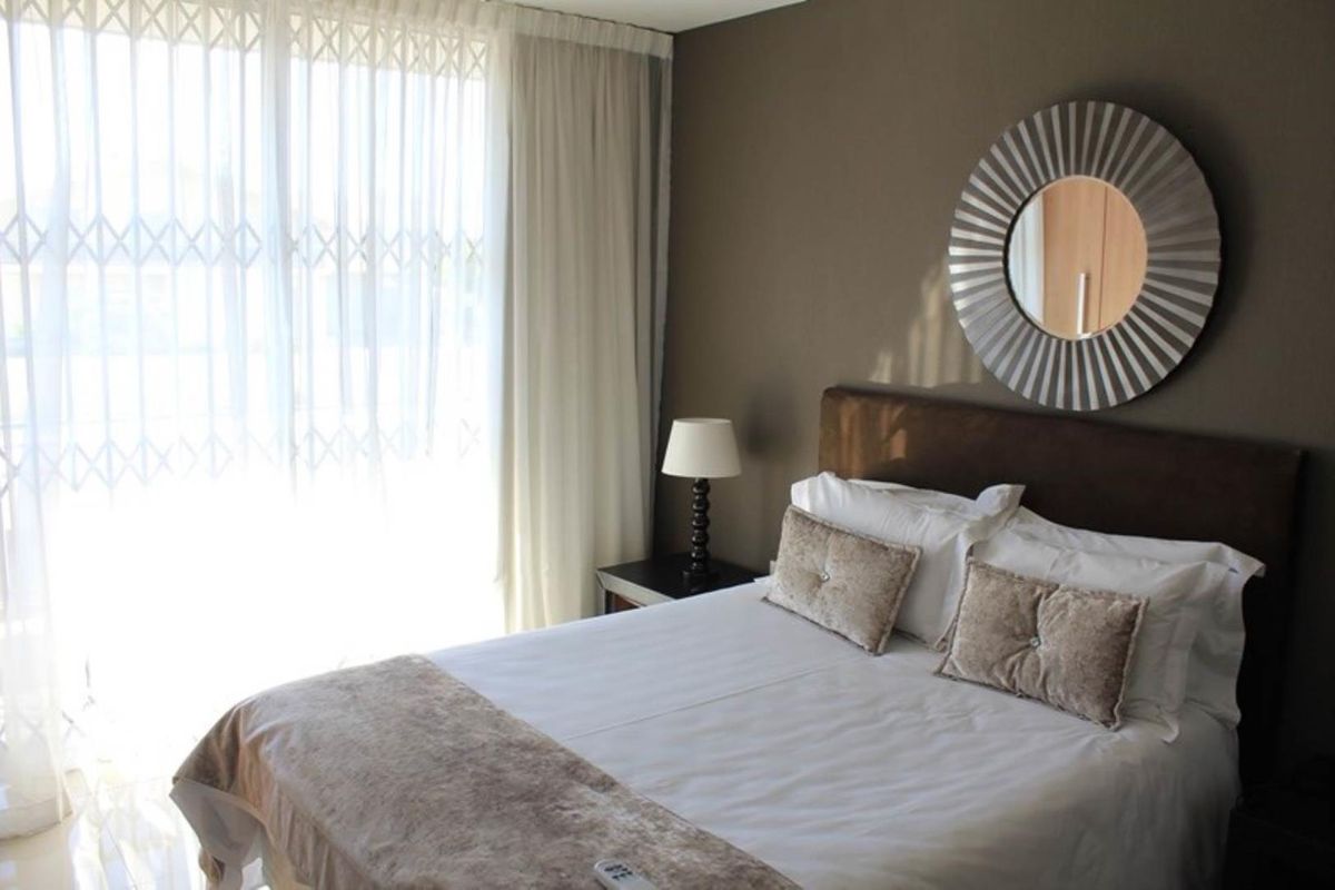 A well-lit bedroom featuring large sliding glass doors with security gates, neutral wall tones, and built-in cupboard space.