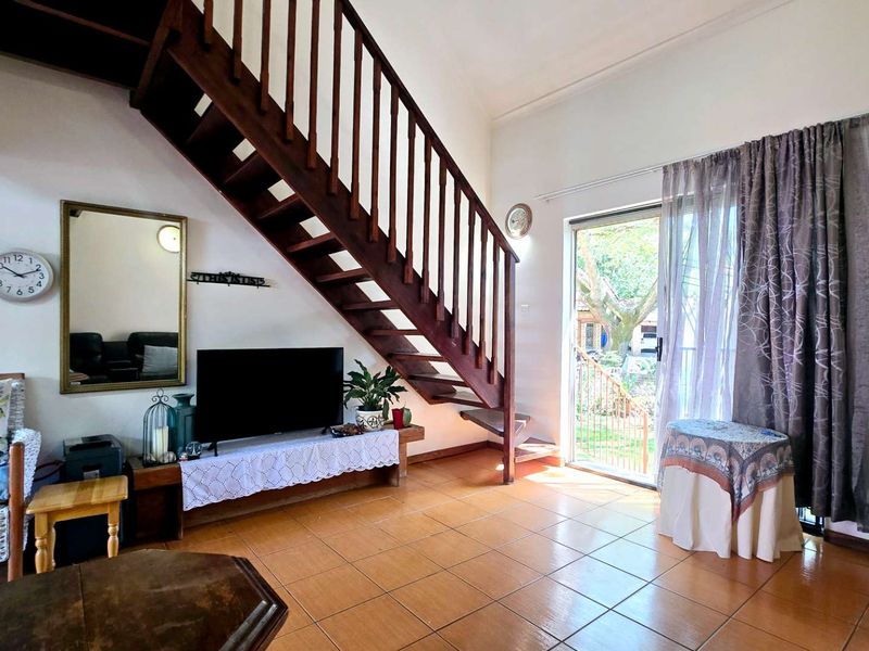 Open-plan living area featuring a wooden staircase, tiled flooring, and a sliding glass door providing access to the outdoor space.