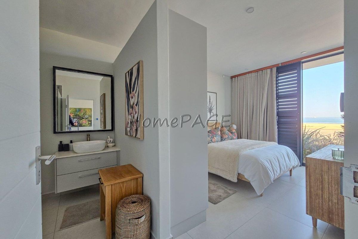 Modern bedroom featuring an open-plan vanity area, tiled flooring, and sliding shutter doors opening to a scenic coastal view.
