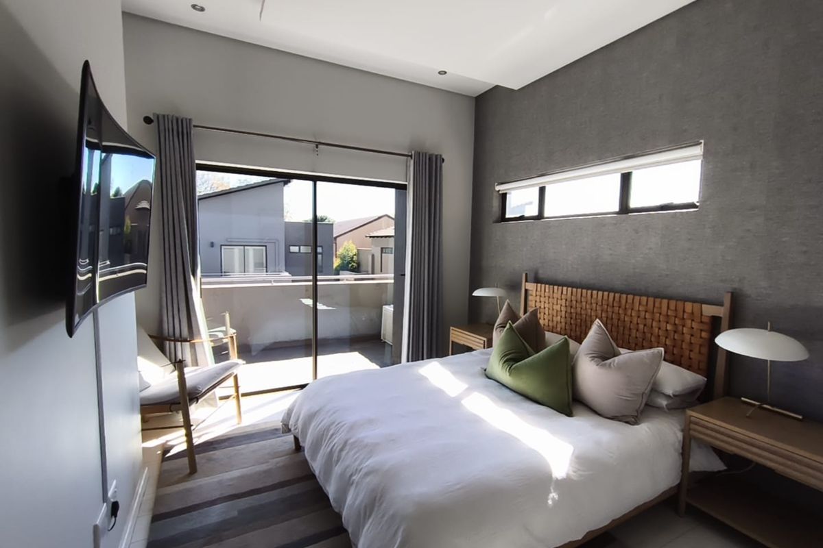 A modern bedroom featuring a textured accent wall, recessed ceiling lighting, and a sliding glass door providing access to a private balcony.