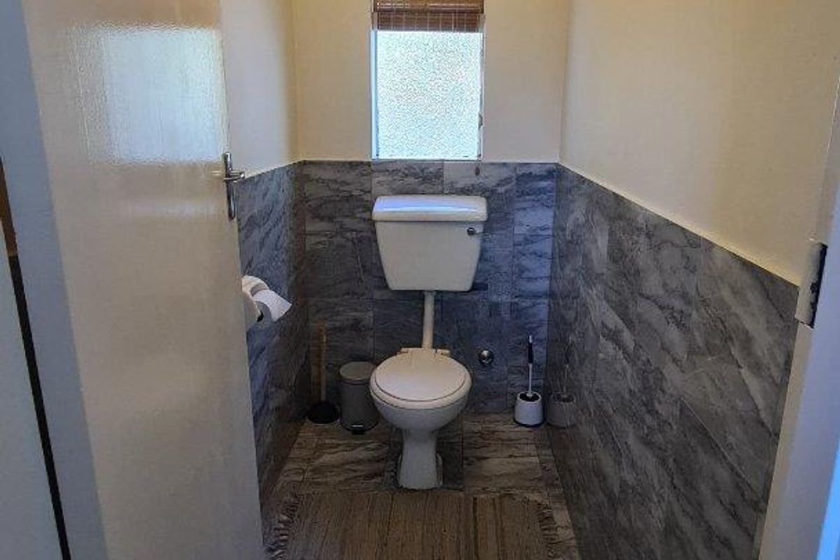 A compact, well-maintained guest bathroom featuring modern grey marble-effect wall and floor tiling, a standard toilet, and a window for natural light.