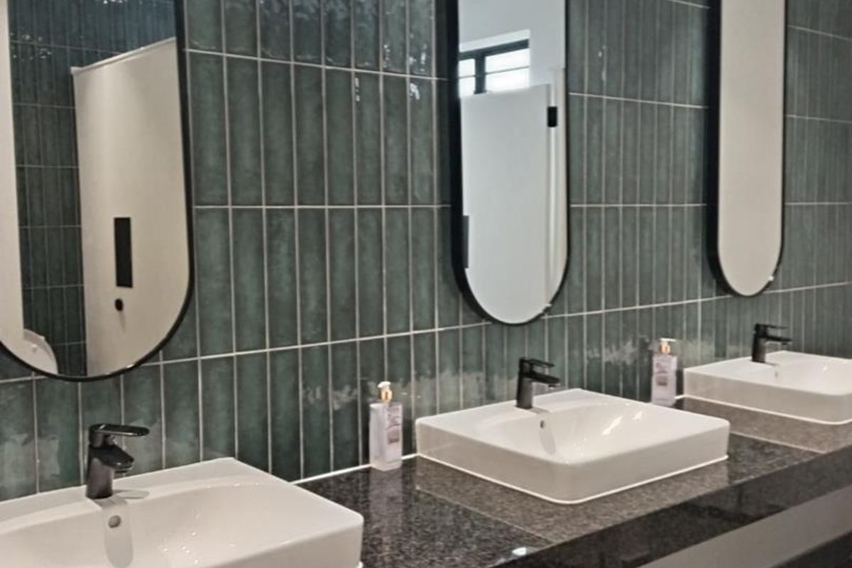 Modern industrial-style bathroom featuring a triple vanity with granite countertop, ceramic vessel sinks, black matte fixtures, and stylish vertical teal subway tiling.