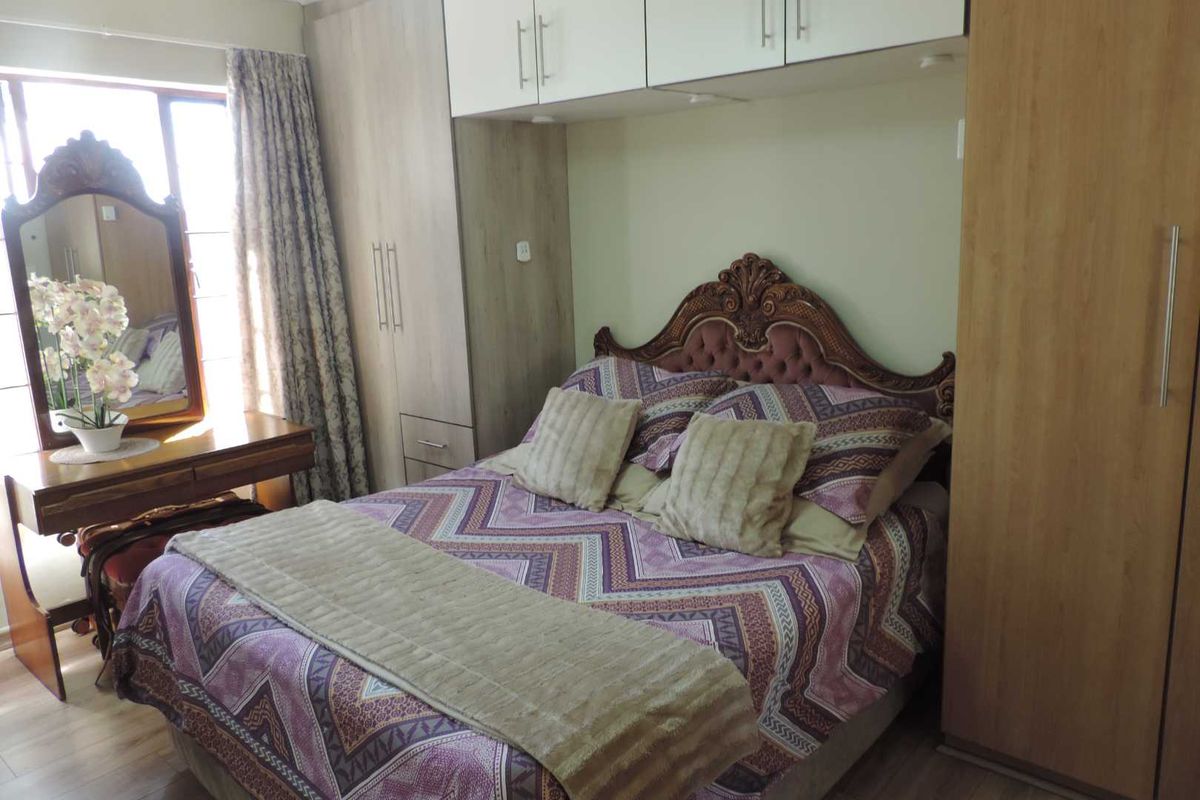 A well-maintained bedroom featuring built-in cupboards, overhead storage units, and laminate flooring, providing ample storage space.