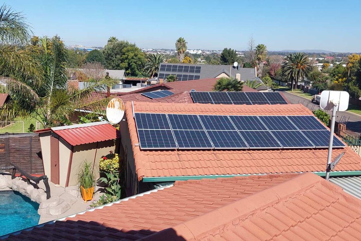An elevated aerial view of the property showing multiple solar panel installations on the tiled roof and a swimming pool in the rear yard.