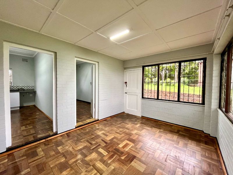 An empty living area featuring classic parquet flooring, painted brick walls, and large windows with security bars, offering a bright and versatile space.