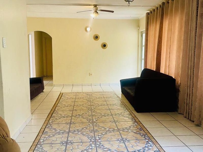 Spacious living room featuring decorative tiled flooring, a ceiling fan, and a classic chandelier, with an archway leading to adjacent areas.