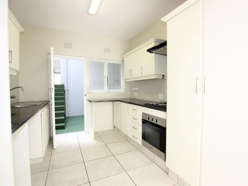 A functional kitchen featuring white cabinetry, granite countertops, a built-in oven with gas hob, and tiled flooring, with direct access to an outdoor area.