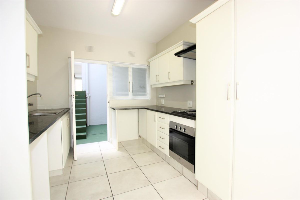 A functional kitchen featuring white cabinetry, granite countertops, a built-in oven with gas hob, and tiled flooring, with direct access to an outdoor area.
