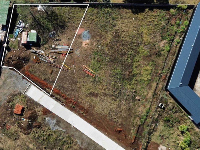 Aerial view of a vacant commercial plot featuring perimeter fencing and a concrete driveway, showing undeveloped land with some surface debris.