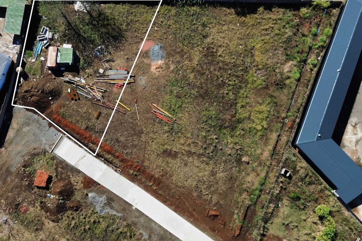 Aerial view of a vacant commercial plot featuring perimeter fencing and a concrete driveway, showing undeveloped land with some surface debris.