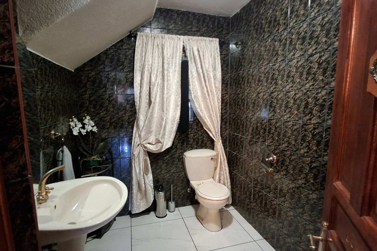 A compact bathroom featuring dark patterned wall tiles, a pedestal basin, and a toilet, situated under a sloped ceiling.
