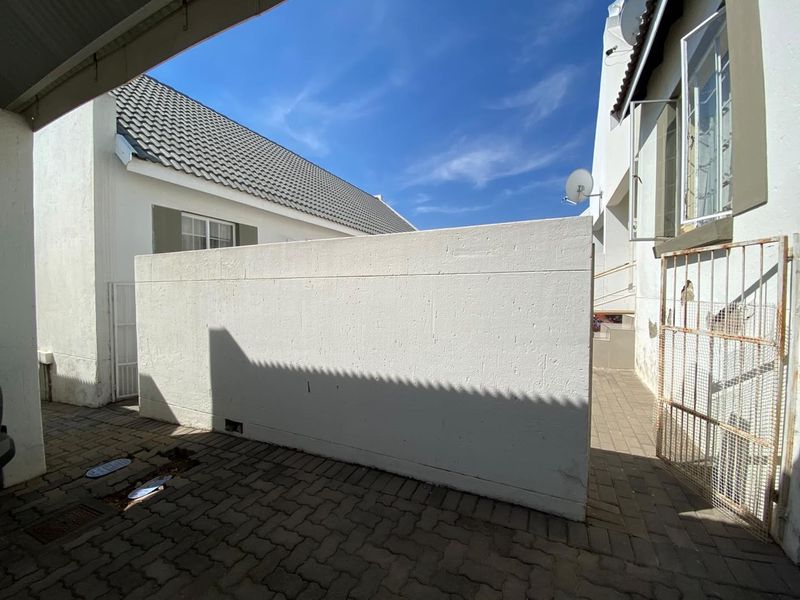 A paved rear exterior area featuring a boundary wall, metal security gate, and satellite dish installation.