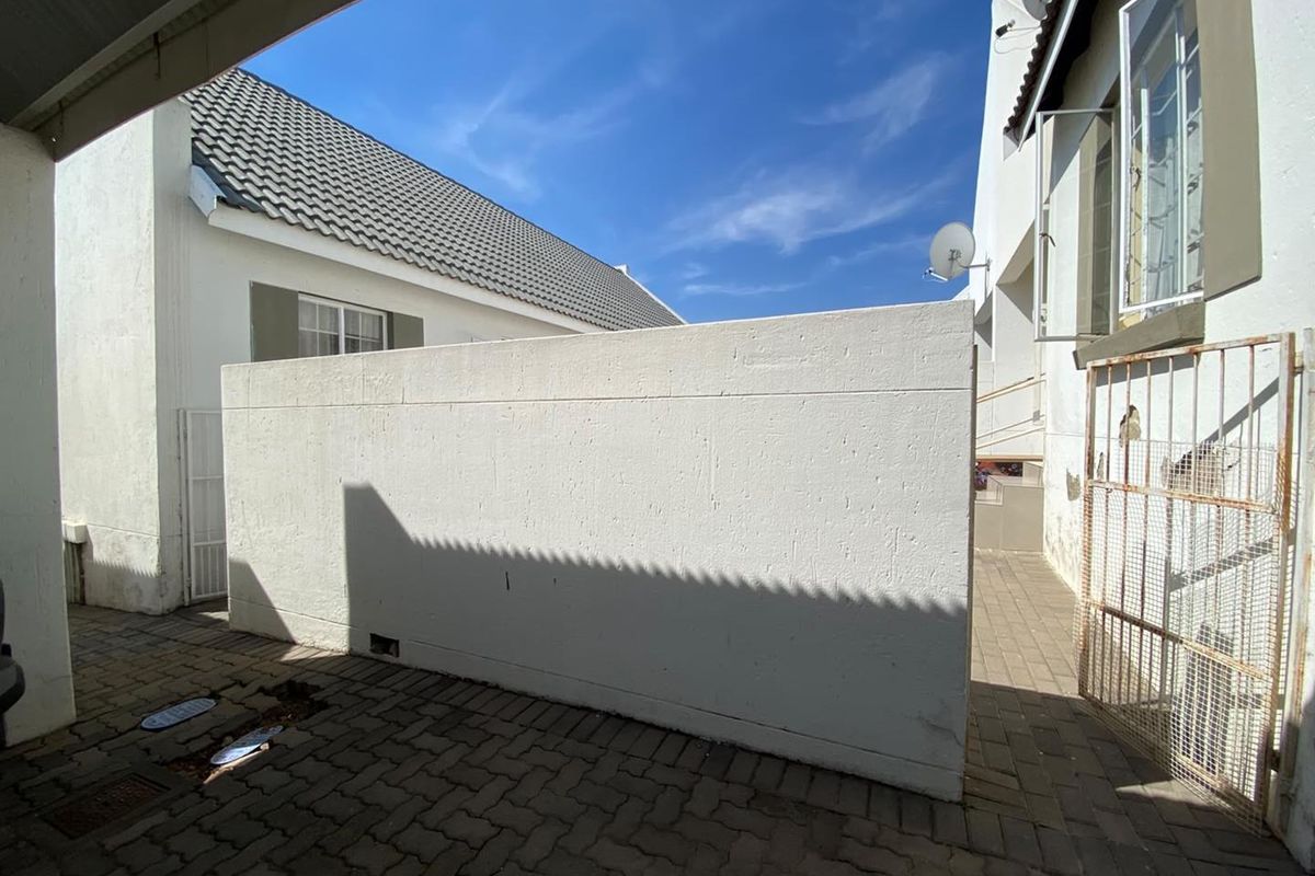 A paved rear exterior area featuring a boundary wall, metal security gate, and satellite dish installation.