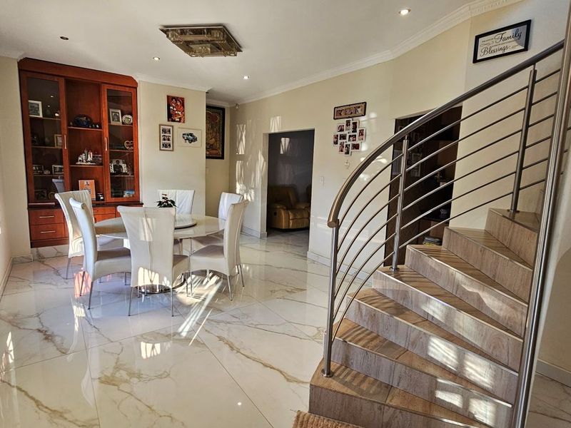 Spacious living and dining area featuring polished marble-look tiled flooring, a striking curved staircase with stainless steel railing, and built-in display cabinetry.